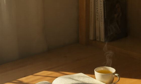 Open book and cup of tea on a wooden desk under warm light, representing the idea of mindful and meaningful reading.