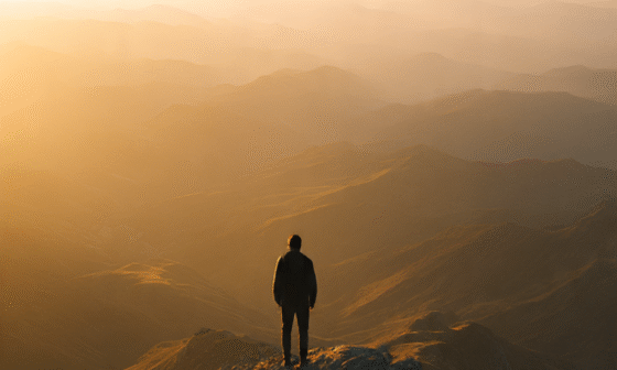 A lone person stands on a mountain peak at sunrise, symbolizing the strength, courage, and sacrifice required to achieve true freedom.