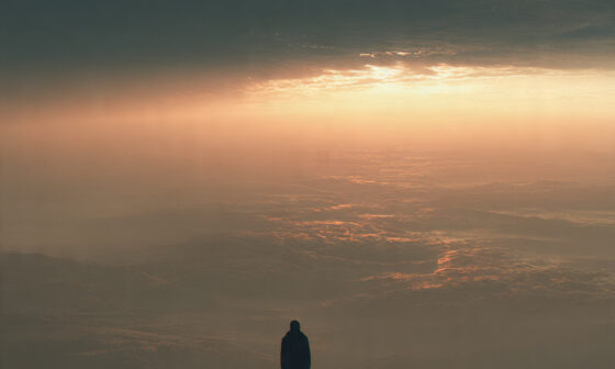 A figure standing on elevated ground at sunrise, symbolizing how changing one’s thinking leads to a higher level of life