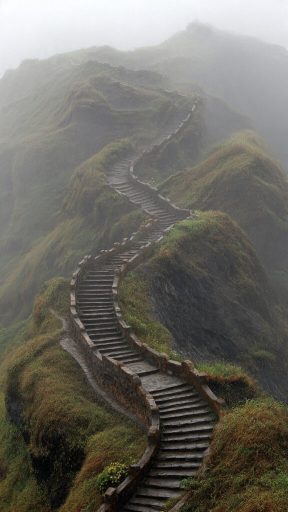 A winding mountain staircase fading into mist, symbolizing commitment to the process rather than obsession with results.