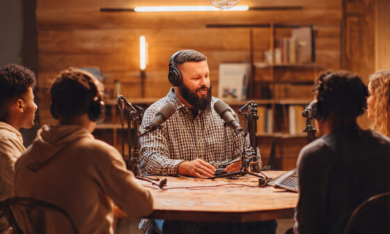 A pastor with beards, seated round a table, like podcast settings with some youths seated with him