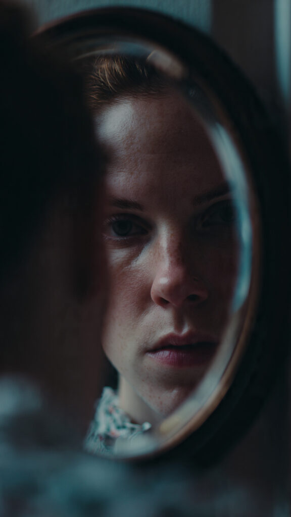 A person looking into a mirror with a serious, reflective expression.