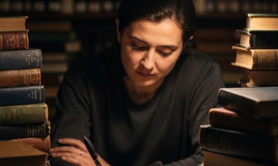 A person sitting at a desk surrounded by books, engaged in deep, focused study and contemplation.